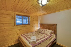 Een houten kamer met een bed, een raam en een plafondlamp.