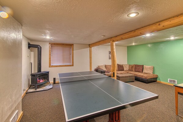 A room with a ping pong table, a wood-burning stove, a green wall, and a sofa.