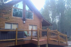 Une cabane en rondins dotée d’une terrasse en bois et d’un escalier menant à une zone abritée.