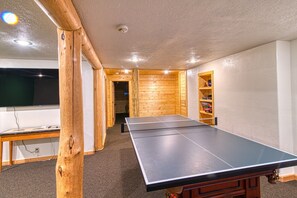 A room with a ping pong table, wooden walls, a ceiling light, and a television.