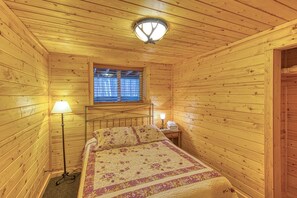 Habitación de cabaña de madera con cama, dos lámparas de noche, ventana con persianas e iluminación en el techo.