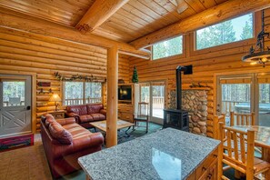 L’intérieur d’une cabane en rondins, avec une cheminée en pierre, un canapé en cuir et un mur d’accent en pierre.