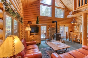 A log cabin interior with a fireplace, leather seating, a television, and a stone wall. - Beautiful Yellowstone Cabin - Hot Tub - Game Room (Island Park)