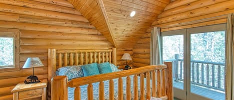 Un dormitorio tipo cabaña de troncos con una cama de madera, dos lámparas de noche, un ventanal y un balcón.