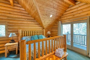 Een slaapkamer in een blokhut met een houten bed, twee bedlampen, een raam en een balkon.