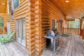 A log cabin with a deck area featuring a grill and outdoor seating.