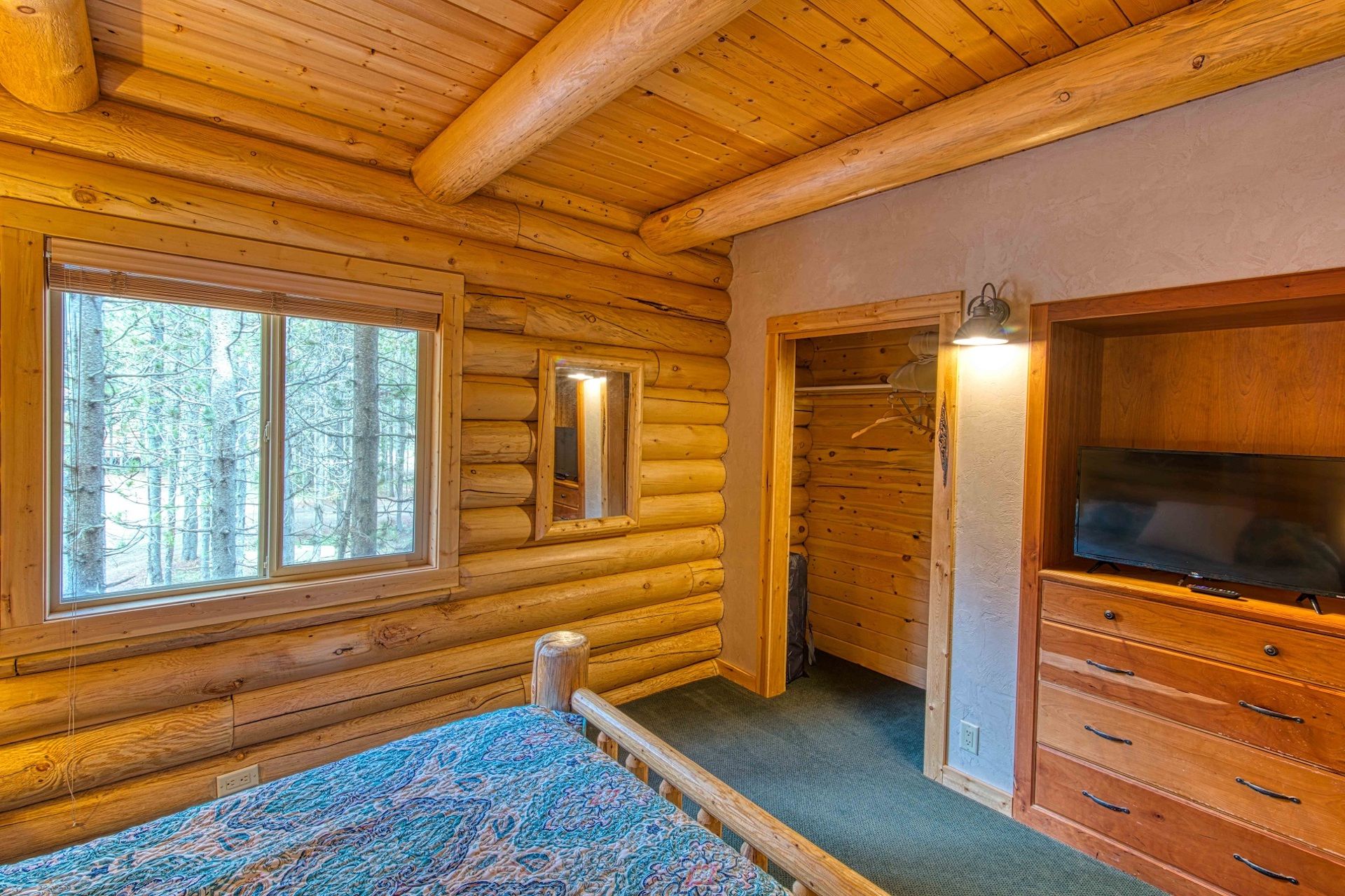 A log cabin interior with a bed, a television, and a large window.