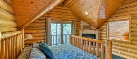 Ein Schlafzimmer in einer Blockhütte mit einem Bett, einem Kamin und einem Fenster mit Blick auf eine Terrasse.