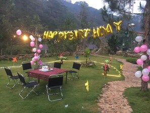 Decoración para una fiesta de cumpleaños al aire libre, con una mesa, sillas y un arco de globos con la inscripción 'HAPPY BIRTHDAY'.