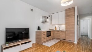 A modern kitchen with white cabinets, a built-in oven, and a large TV on a wooden stand. - Teatr Wielki 2-Bedroom Apartment (Warsaw)
