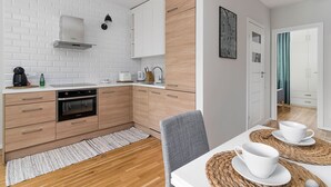 A modern kitchen with white brick backsplash, wooden cabinets, stainless steel appliances, and a dining area with a table set for two. - Teatr Wielki 2-Bedroom Apartment (Warsaw)