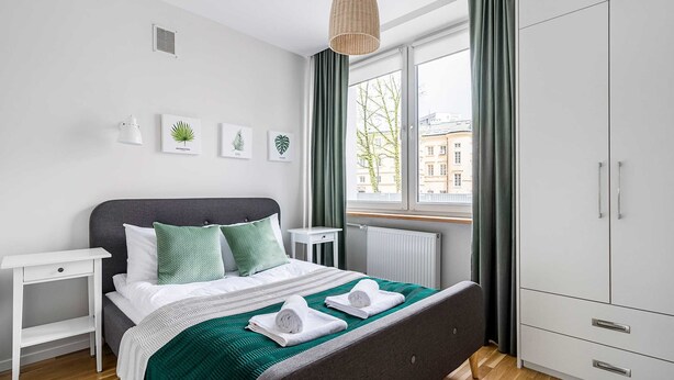 A modern bedroom with a bed, bedside tables, a wardrobe, and a window with curtains. - Teatr Wielki 2-Bedroom Apartment (Warsaw)