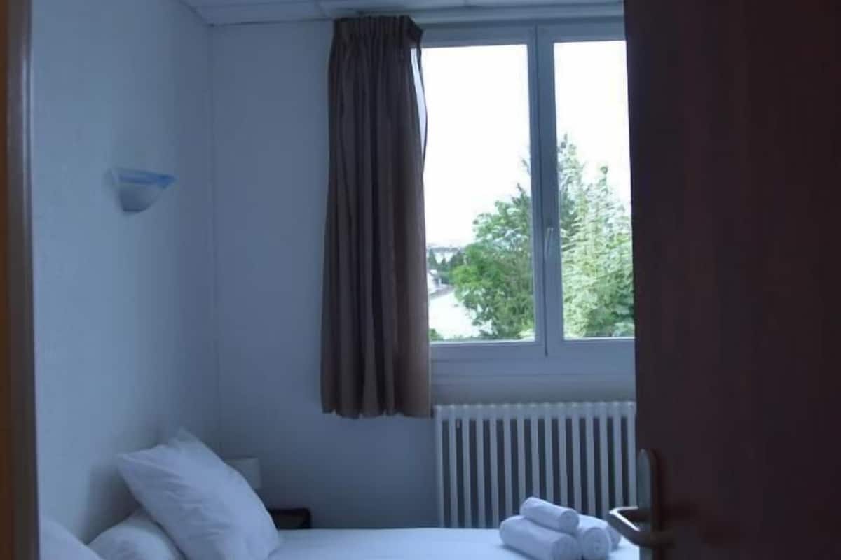 Une chambre avec deux lits, une fenêtre avec des rideaux, un ventilateur de plafond et un radiateur.
