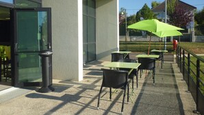 An outdoor patio with tables and chairs, a trash bin, and a green umbrella. - Sofratel (Joigny)