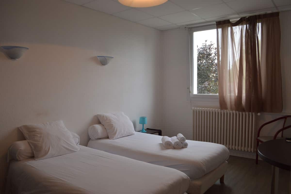 Une chambre d’hôtel avec deux lits, une fenêtre avec des rideaux, une table et une chaise.
