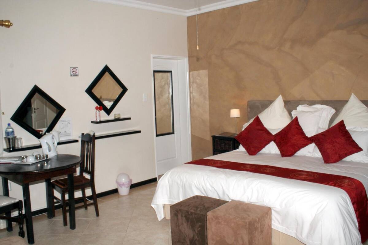 A hotel room with a bed, a desk with a chair, a small table, and two wall-mounted mirrors.