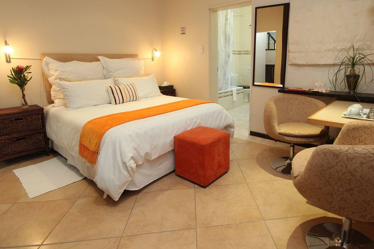 A hotel room with a bed, bedside table, nightstand, chair, and a small table with a plant.
