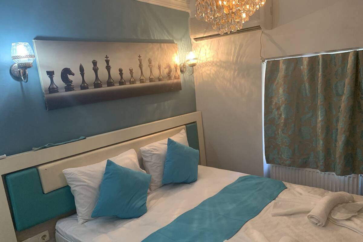 A neatly made bed with white and blue bedding, a chessboard on the wall, and a chandelier.