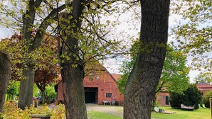 Un bâtiment en briques surmonté d’un toit rouge, entouré d’arbres et d’une clôture en bois.