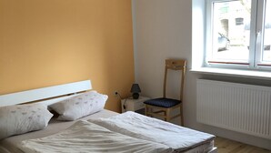 Un dormitorio con cama, silla, lámpara y ventana.