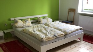 Un dormitorio con cama, mesita de noche, silla y ventana.