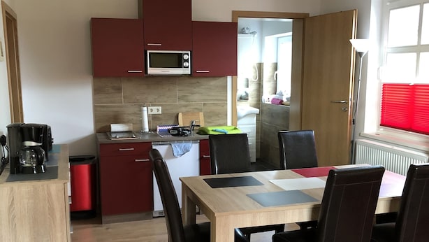 Una cocina compacta con microondas, cafetera y comedor con mesa y sillas.