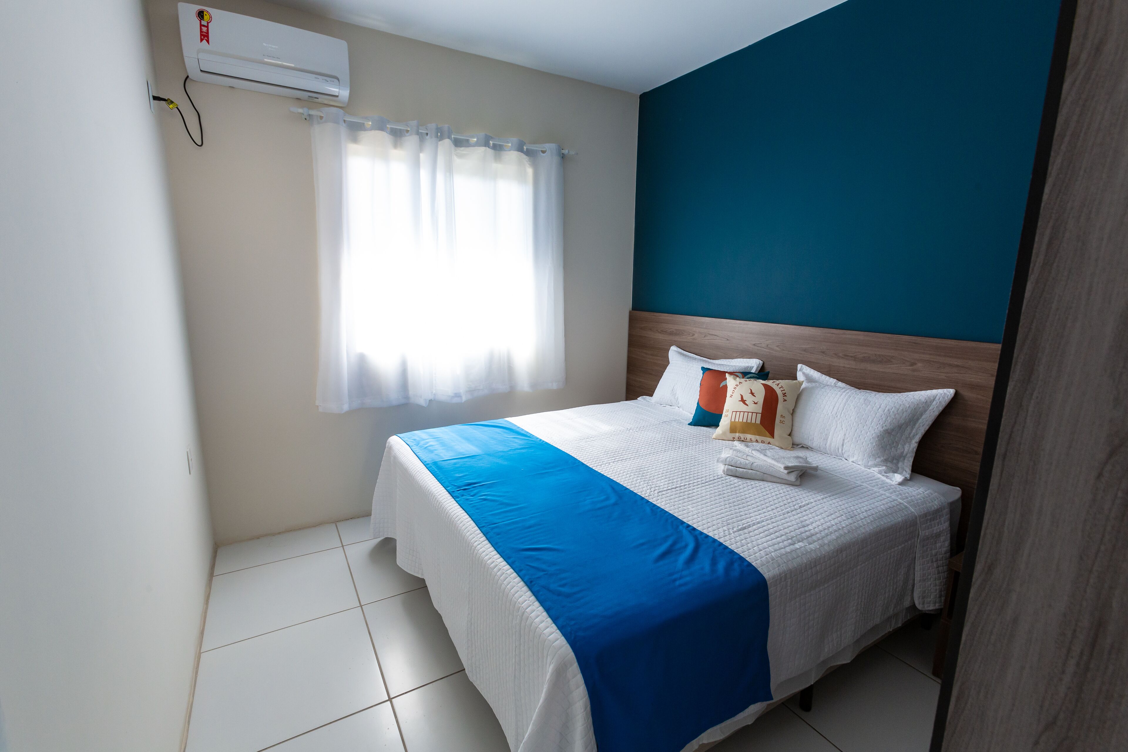 A neatly made bed with a blue and white bedspread, a white pillow, and a wooden headboard.