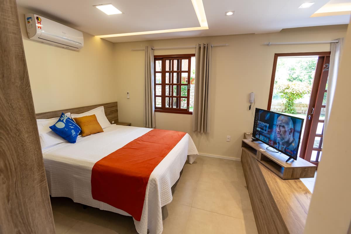 Une chambre d’hôtel équipée d’un lit, d’une télévision, d’une fenêtre avec des rideaux et d’un appareil de climatisation.