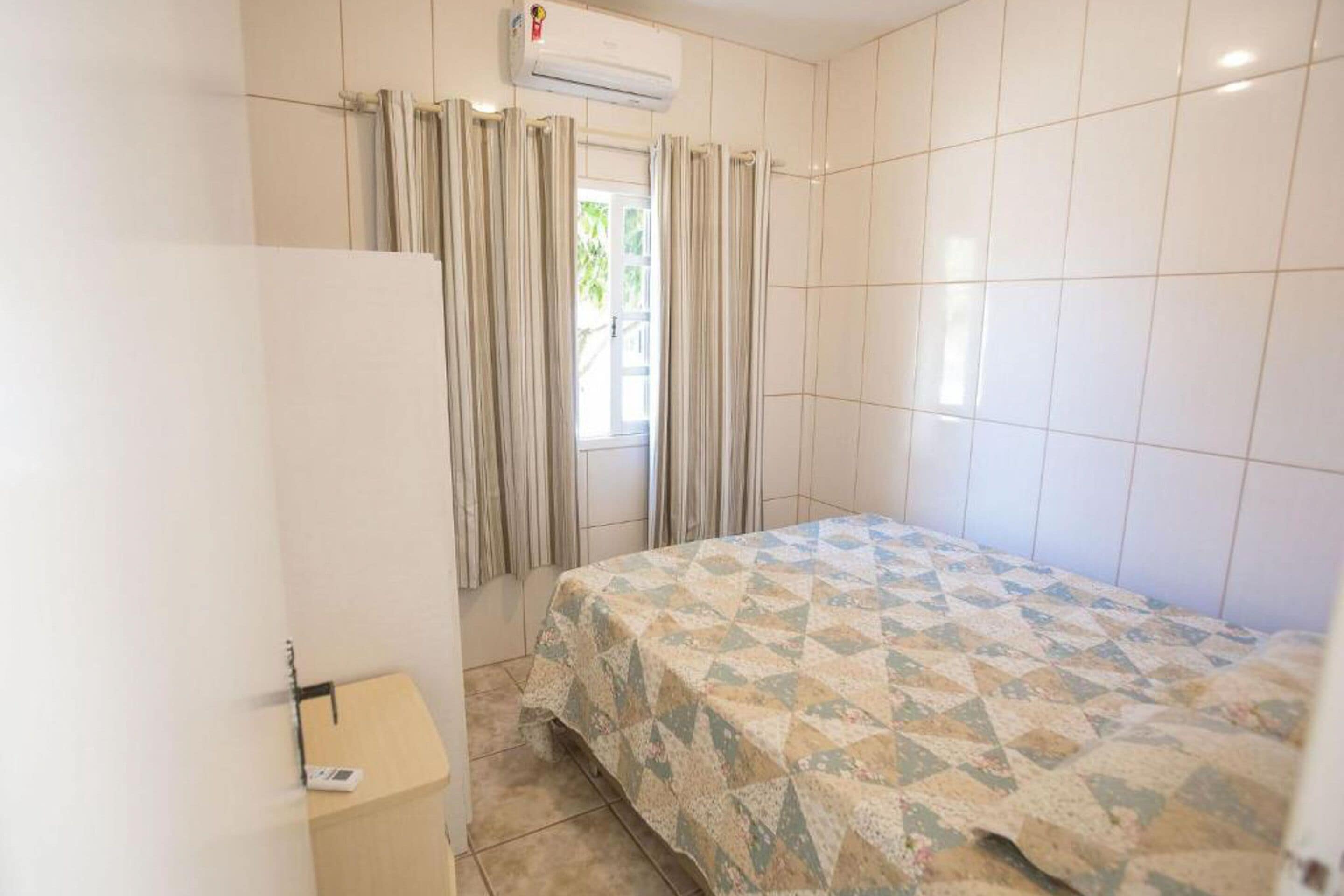 Une chambre à coucher avec un lit, des rideaux, un appareil de climatisation et une petite armoire en bois.