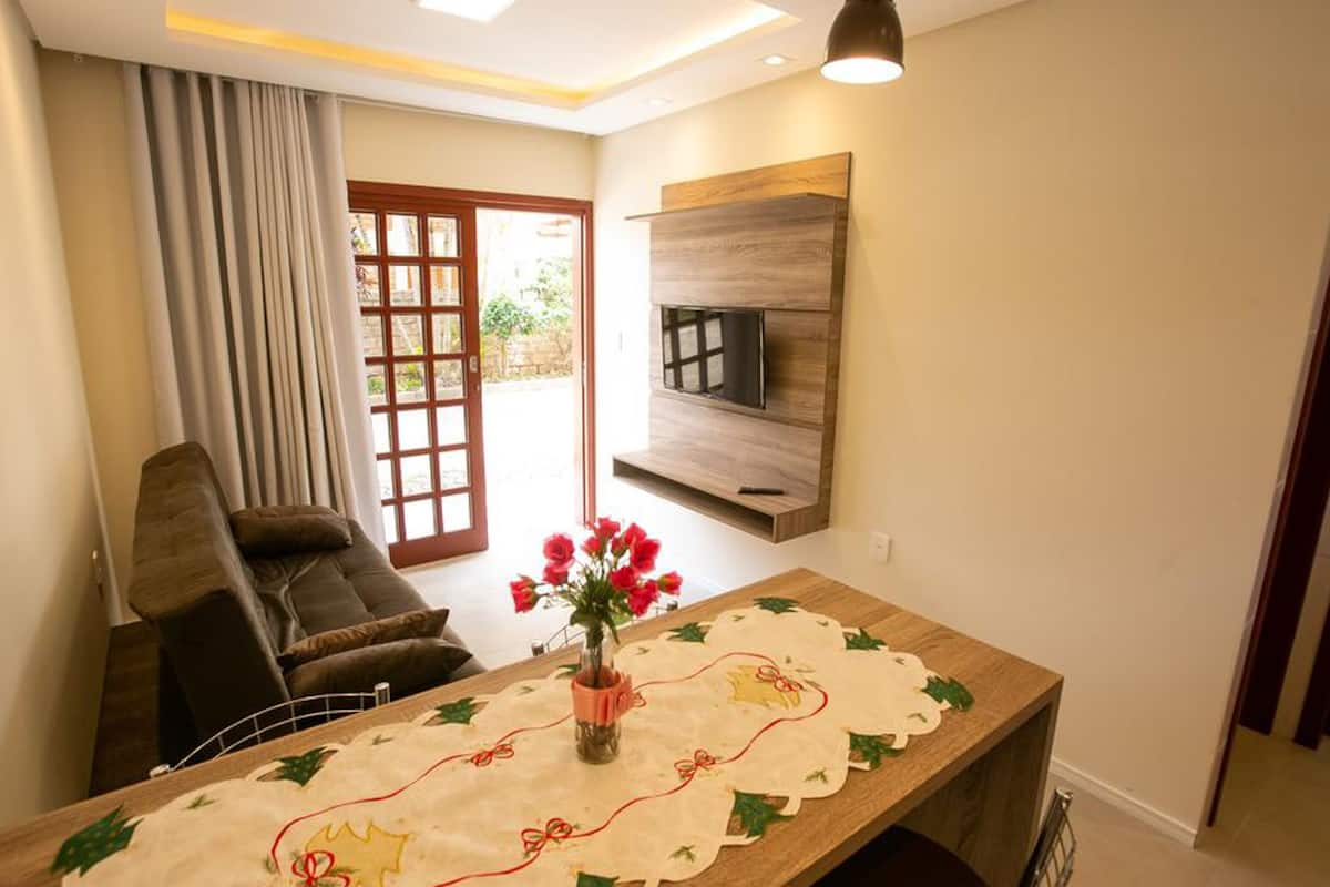 Un salon moderne comprenant un canapé, une table basse agrémentée d’un chemin de table décoratif, un vase avec des fleurs et un téléviseur à écran plat fixé au mur.