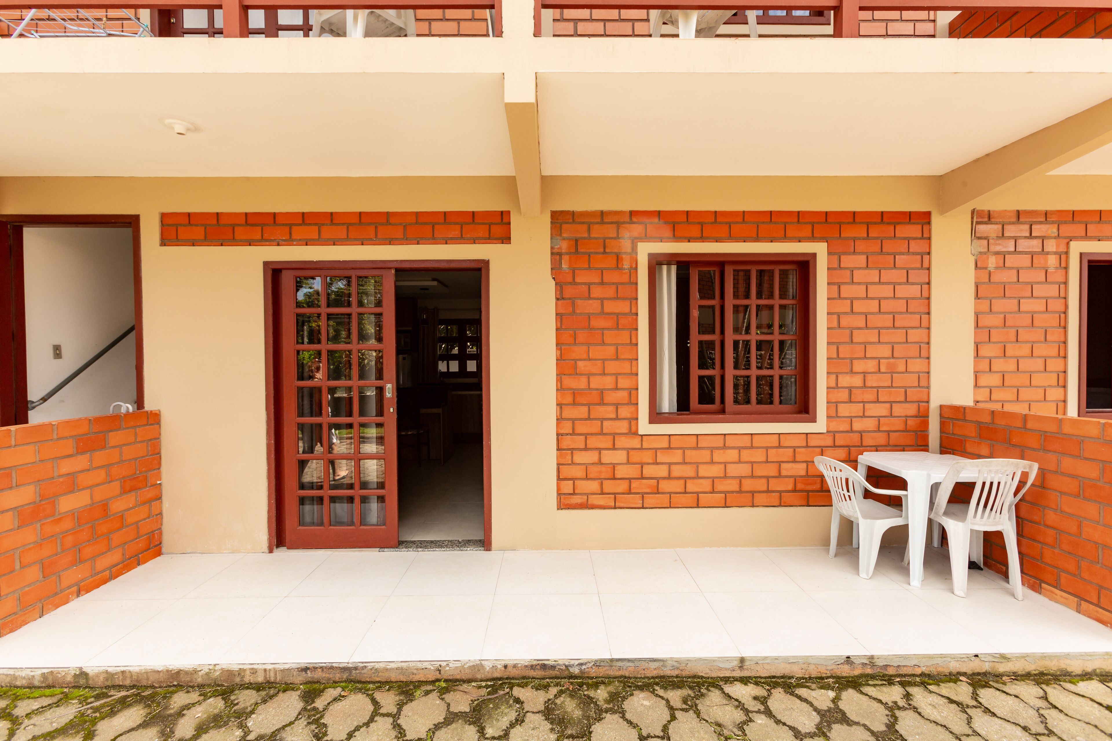 Un bâtiment à deux étages avec une façade en briques, un balcon et un patio aménagé avec une table et des chaises.