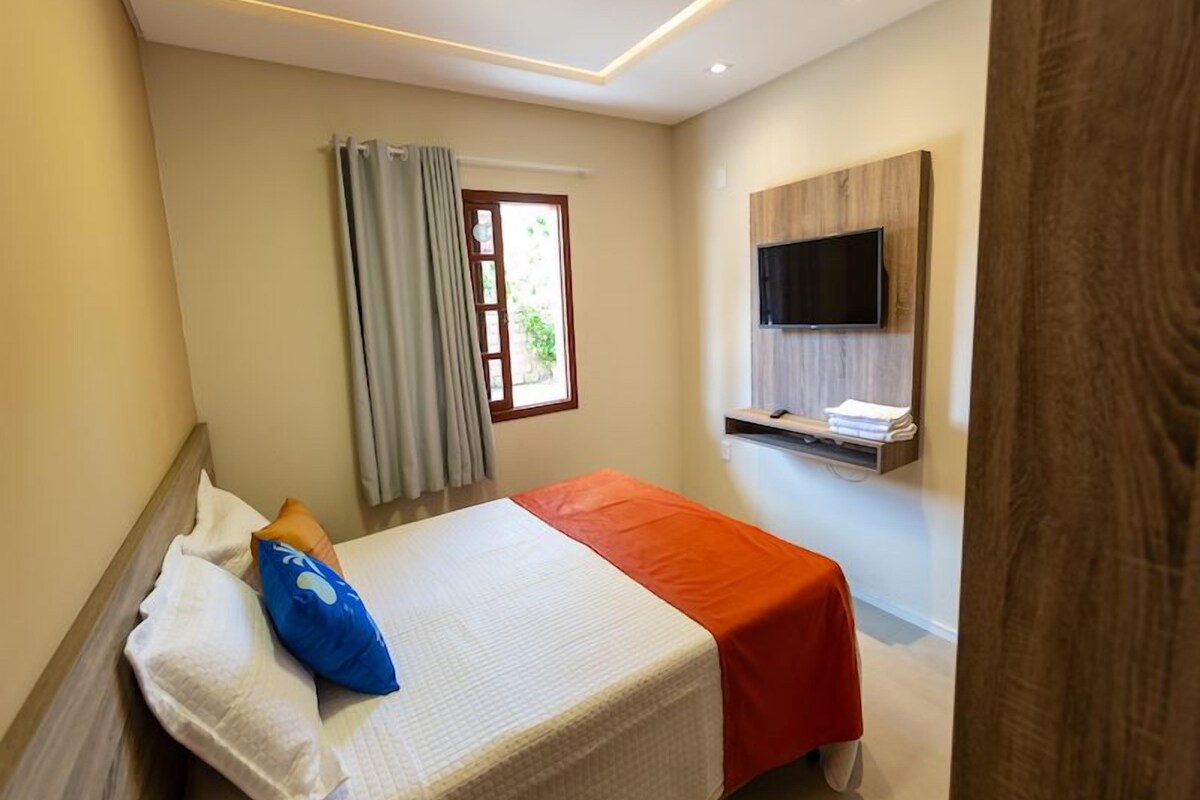A hotel room with a bed, a TV mounted on the wall, and a window with curtains.
