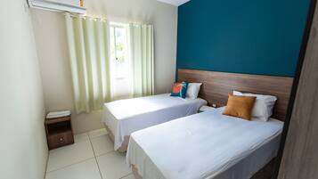 Habitación de hotel con dos camas, una ventana con cortinas, cabecera de madera y una mesita de noche de madera.