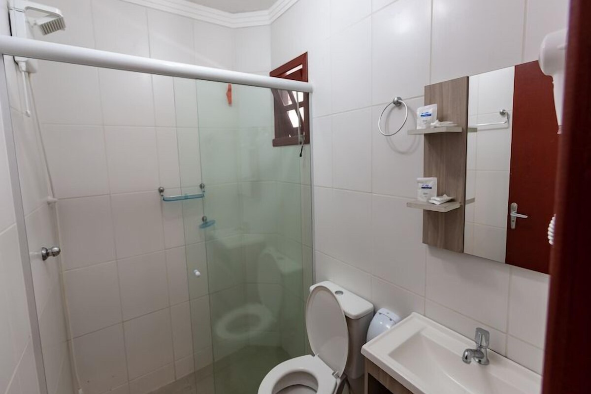 A bathroom with a glass shower enclosure, a toilet, a sink, and a mirror.
