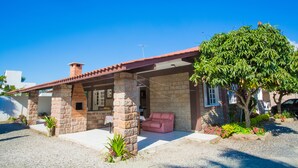 Une maison en pierre avec un toit recouvert de tuiles rouges, un patio abrité et un canapé rose.