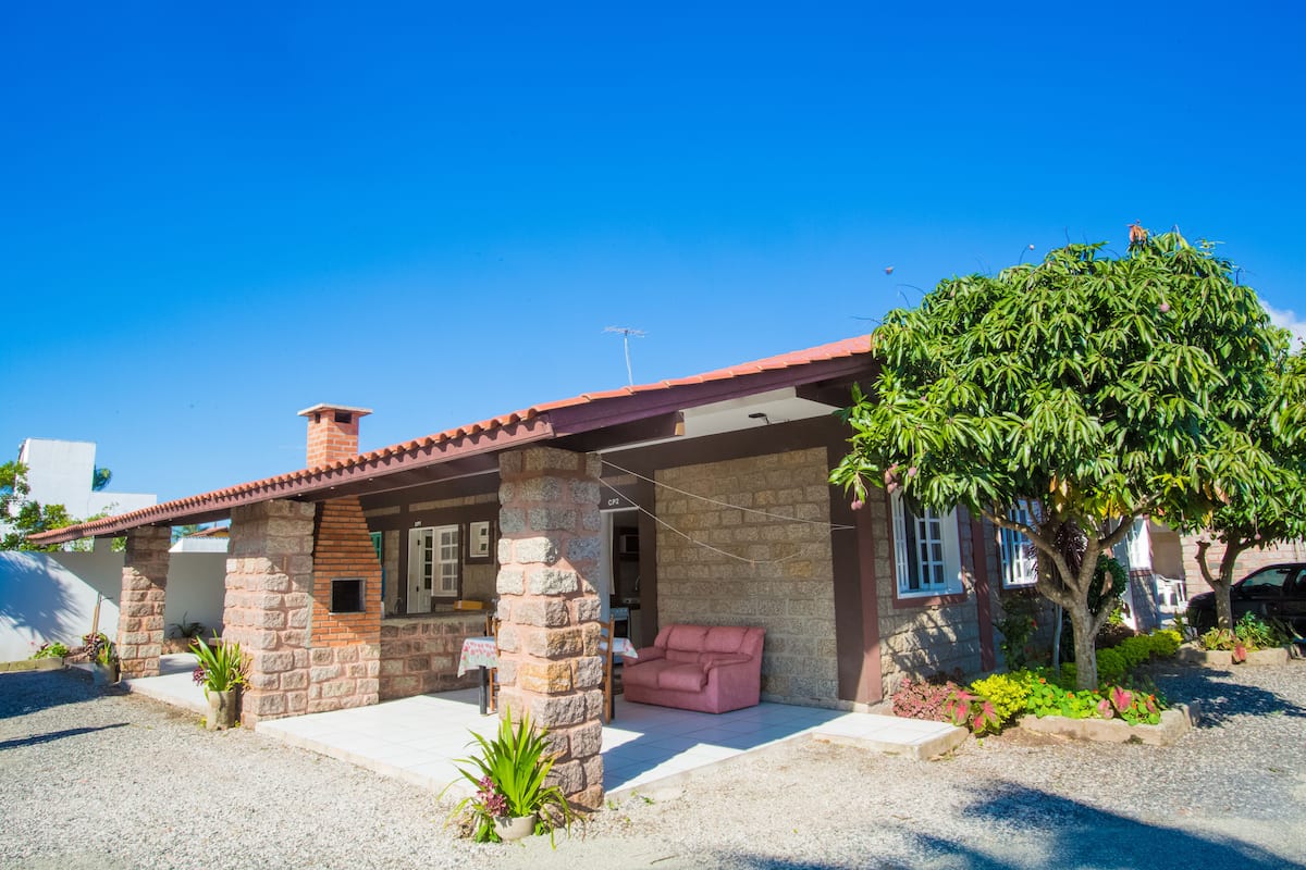 Une maison en pierre avec un toit recouvert de tuiles rouges, un patio abrité et un canapé rose.