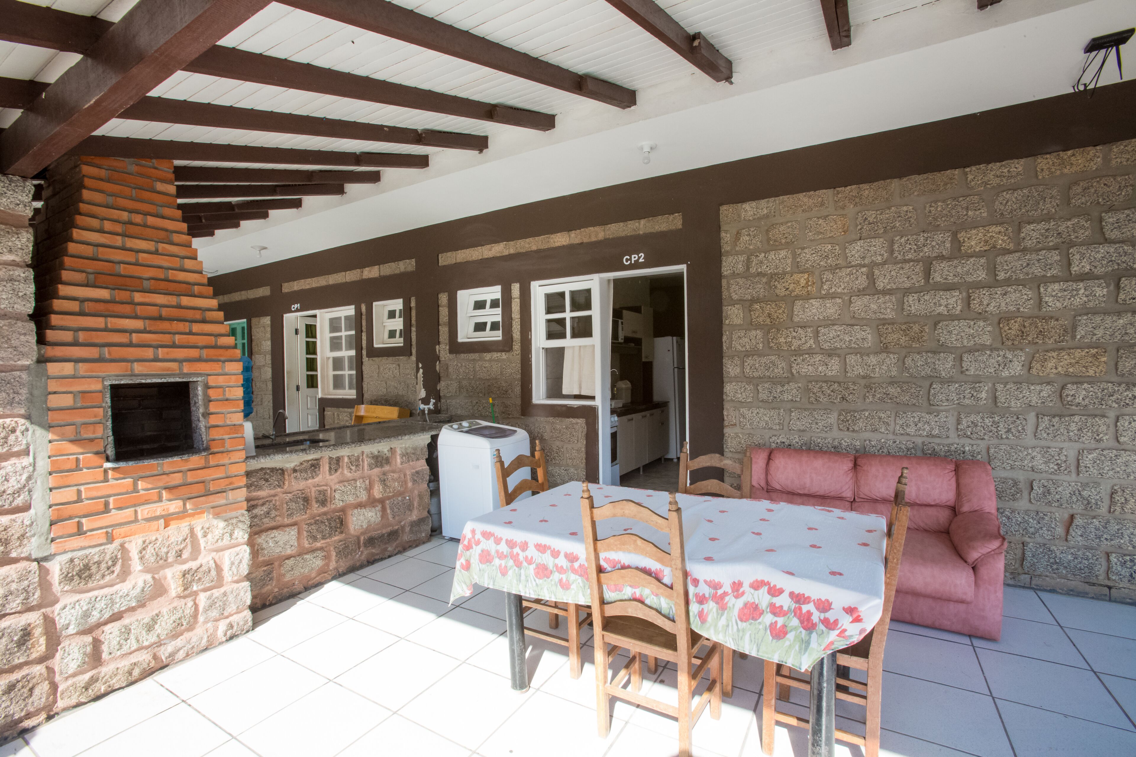 A covered patio with a brick fireplace, a dining table with chairs, and a pink sofa.