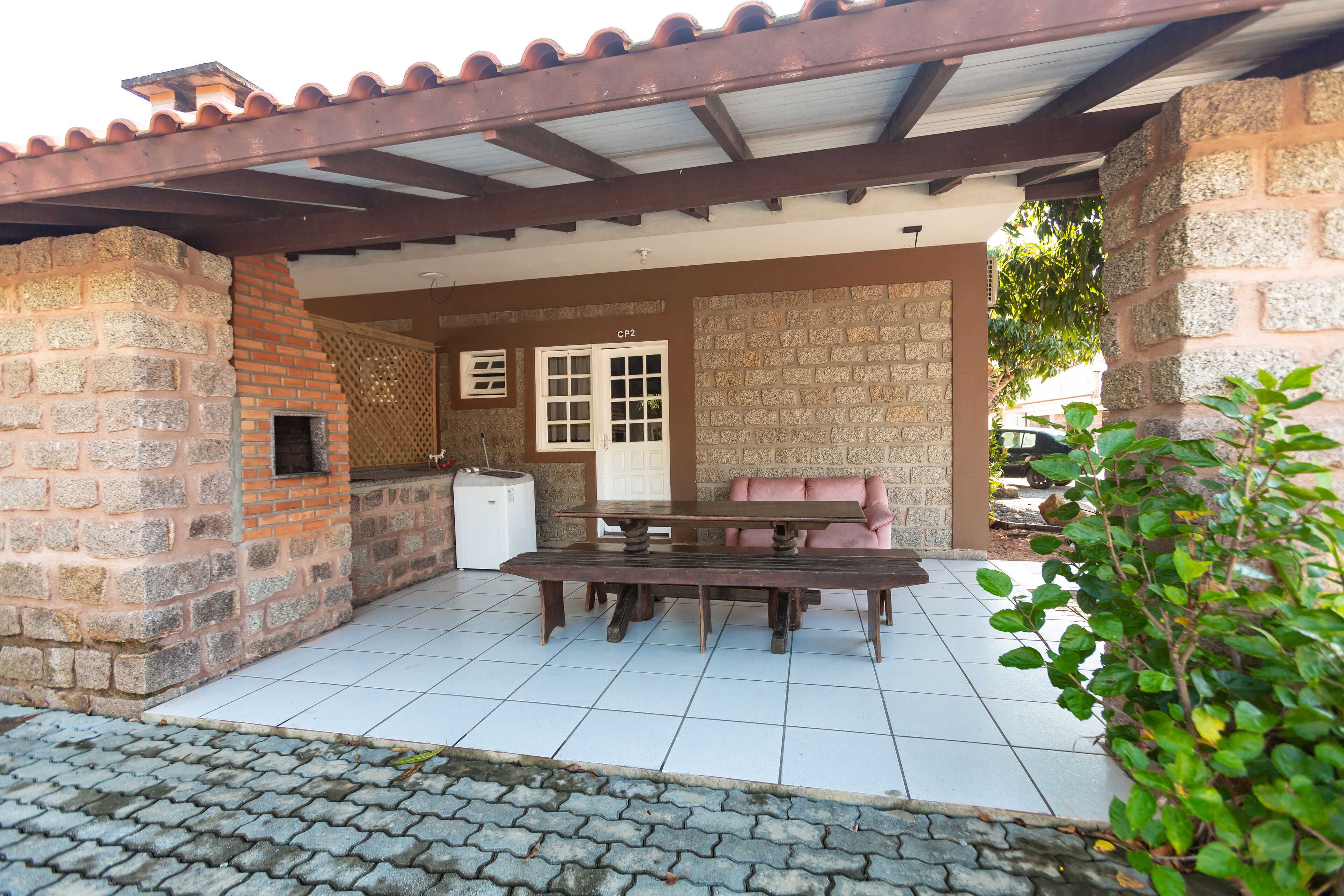 Un patio cubierto con muro de piedra, horno de ladrillo, refrigerador blanco, mesa de madera y sofá rosa.