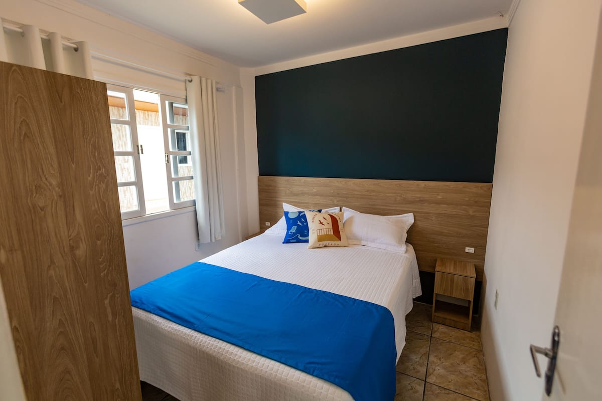 Une chambre d’hôtel avec un lit, une table de chevet, une porte en bois et une fenêtre avec des rideaux.