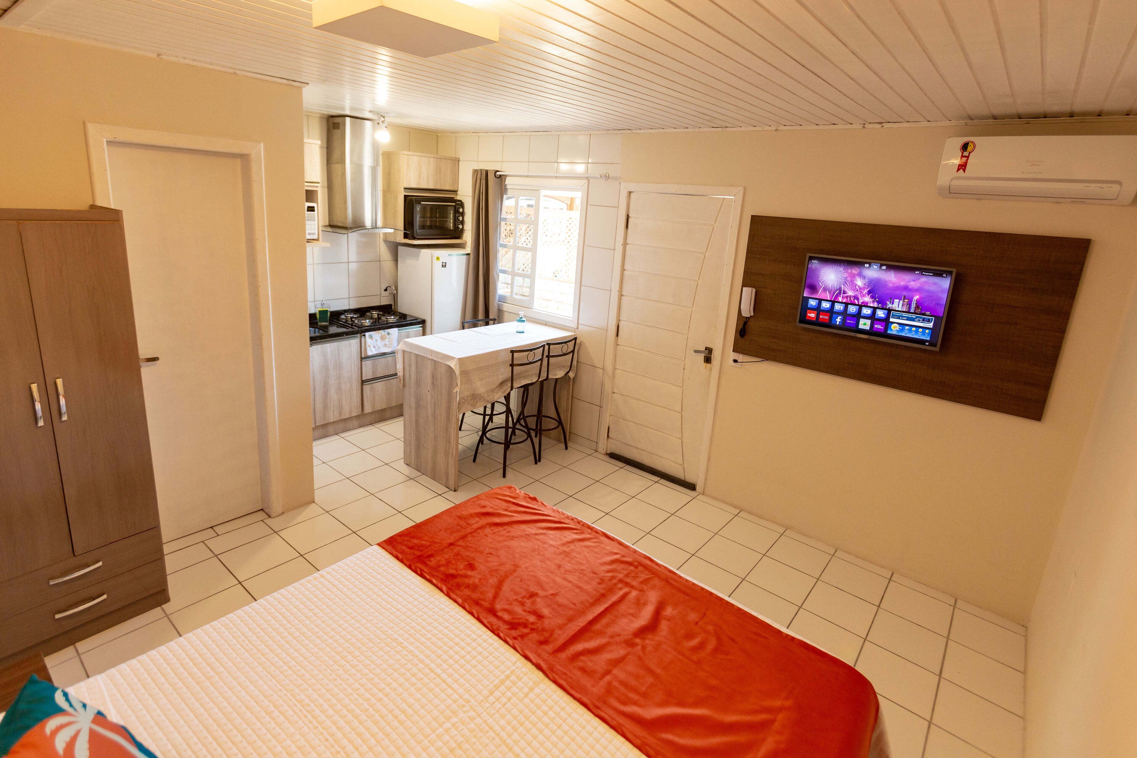 A compact room with a bed, a kitchenette, and a TV mounted on the wall.