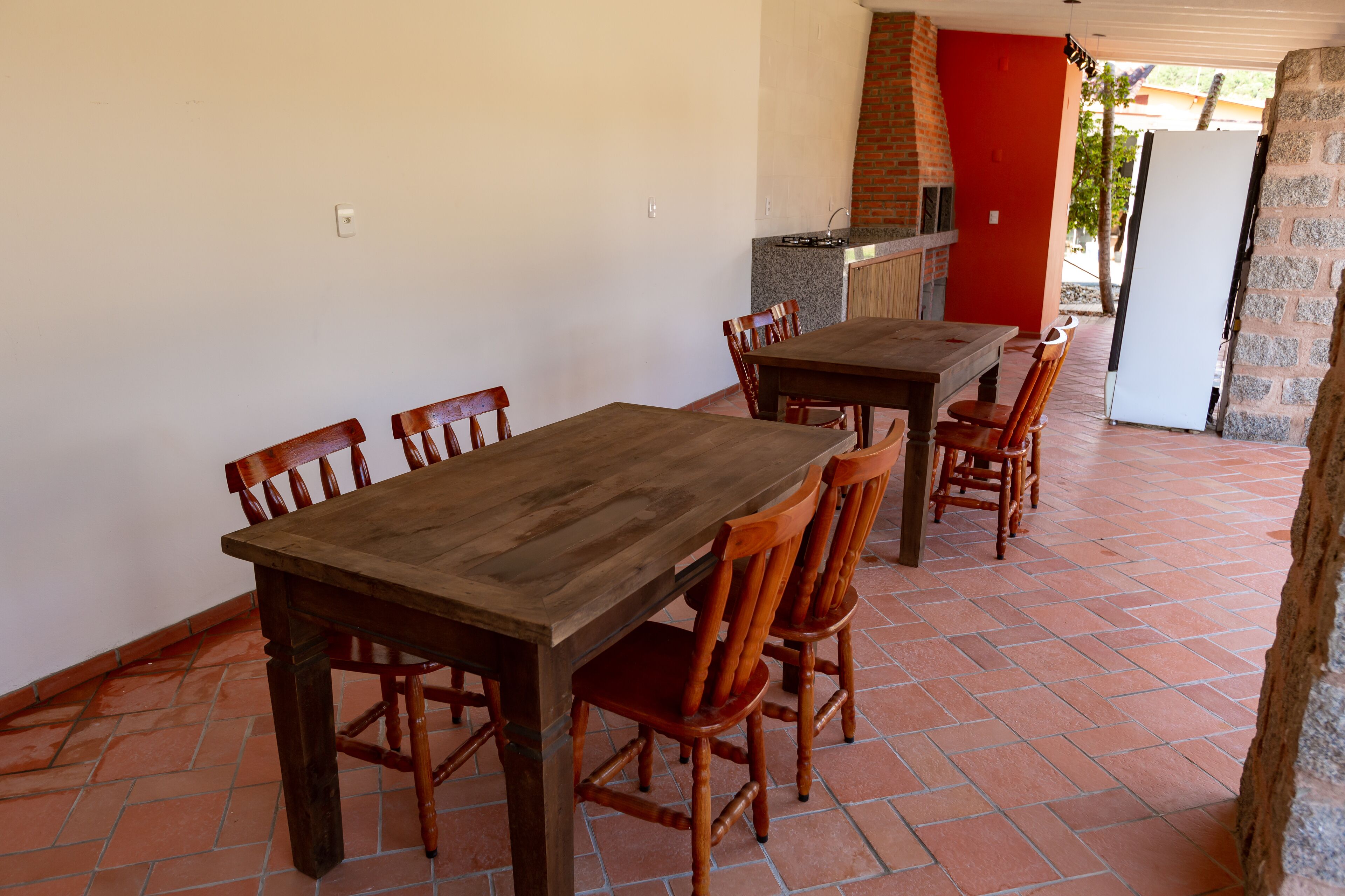 Zona pranzo con tavolo e sedie in legno, parete in mattoni e una porta rossa.