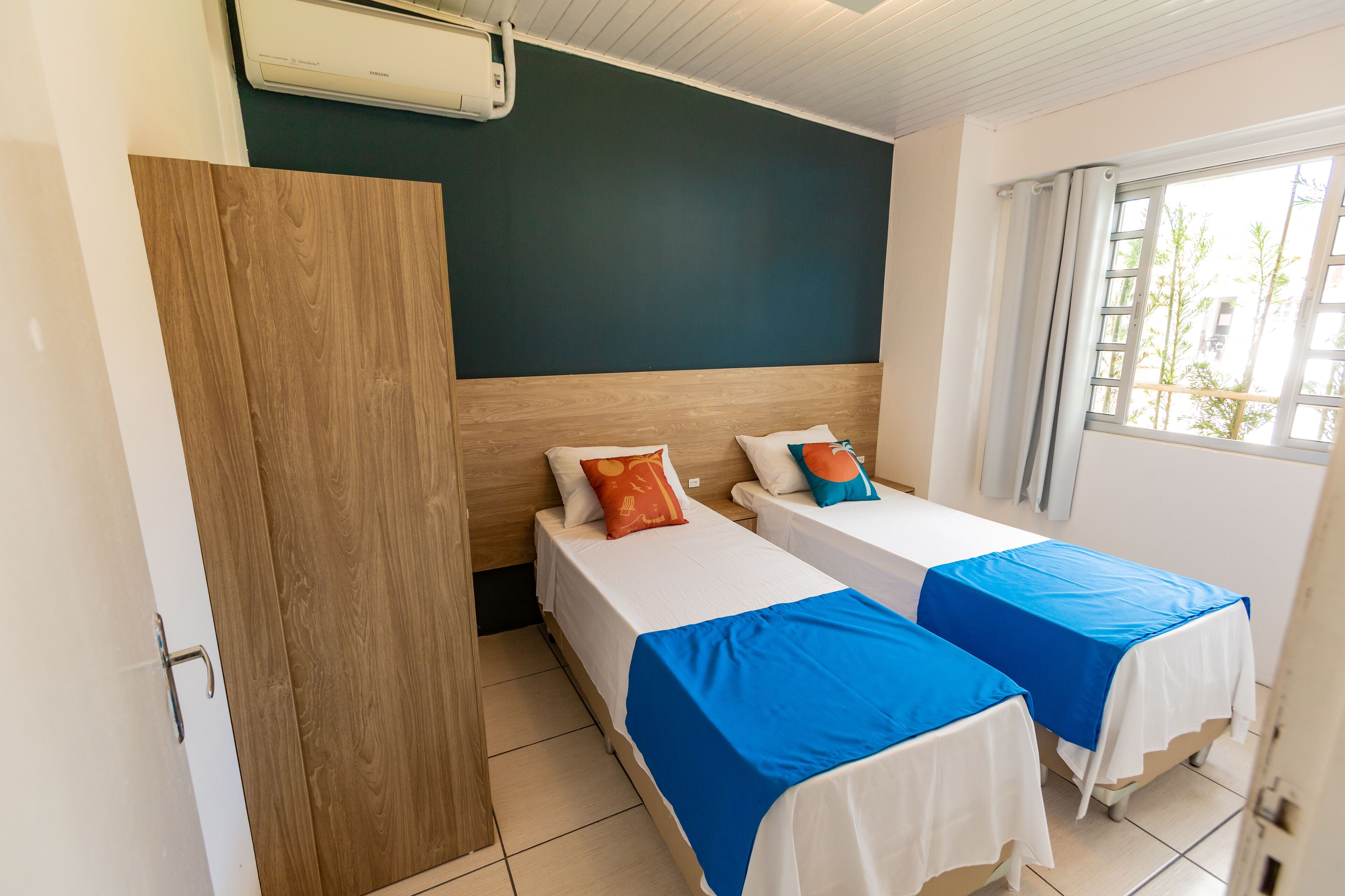Habitación de hotel con dos camas, un armario de madera, ventilador de techo y ventana con cortinas.