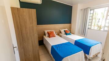 Habitación de hotel con dos camas, un armario de madera, ventilador de techo y ventana con cortinas.