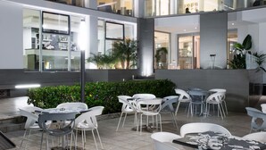 A modern indoor courtyard with multiple seating areas, glass walls, and indoor plants. - Hotel Excelsior (Alba Adriatica)