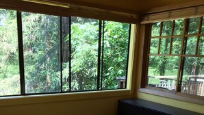Un dormitorio con una cama grande, una ventana que da a zonas verdes y una mesita cerca de la ventana.