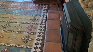 Una sala de estar acogedora con un tapete estampado, chimenea y un ventanal con vistas a la vegetación.