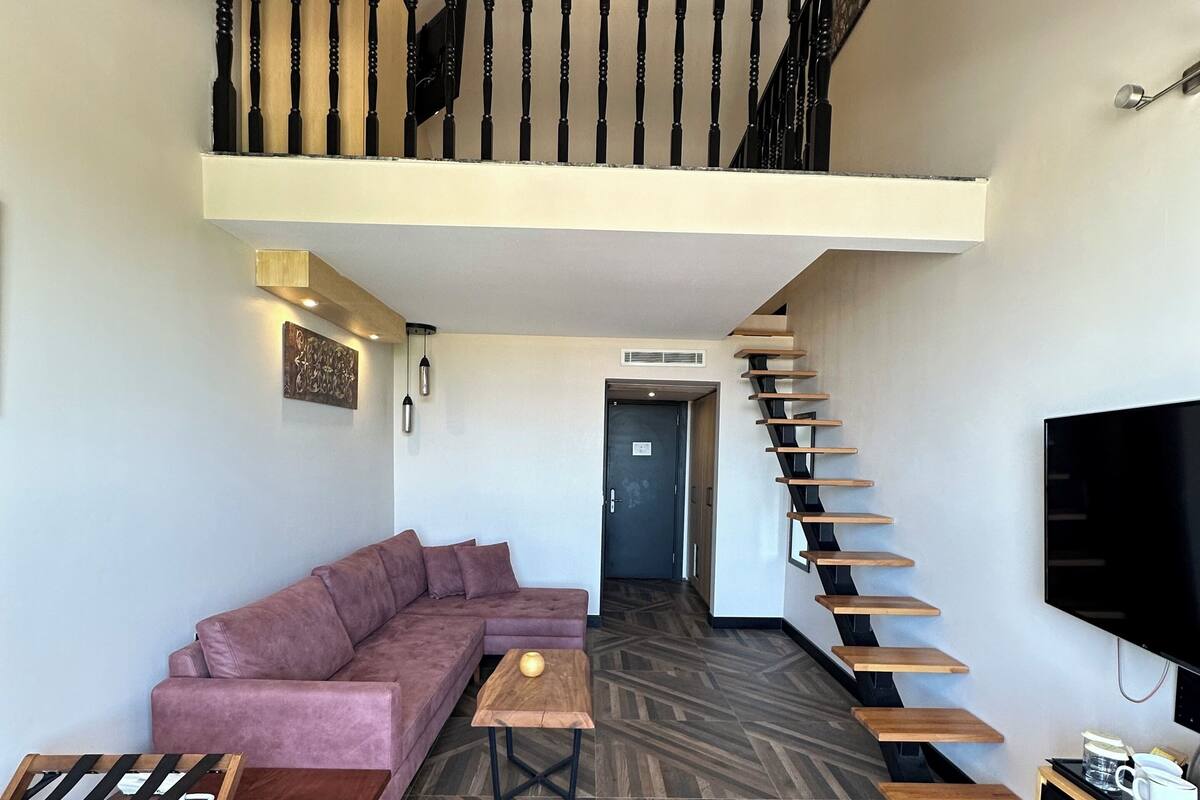 Een moderne woonkamer met een bank, een salontafel en een televisie. Een trap leidt naar een hoger gelegen niveau.