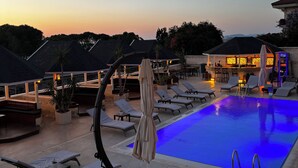 Un espace aménagé au bord de la piscine, avec des chaises longues, une piscine et un bar doté d’un éclairage d’ambiance.