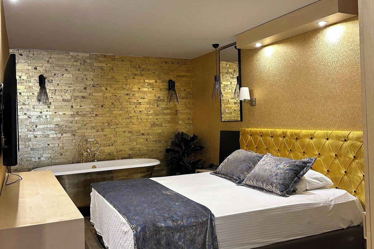 Een moderne slaapkamer met een bakstenen muur, een bed met een geel hoofdeinde, een nachtkastje en een bureau met een stoel.
