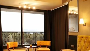 Habitación de hotel con cama, escritorio, dos sillas, una mesa, balcón con vistas y un espejo grande.